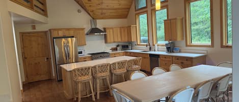 Una cocina amplia con armarios de madera, una isla grande con taburetes de bar y varias ventanas que ofrecen luz natural.