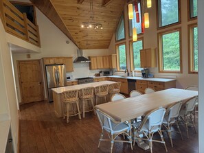 A spacious kitchen with wooden cabinets, a large island with bar stools, and multiple windows providing natural light. - Mainland St. Lawrence River Home with Private Dock (Alexandria Bay)