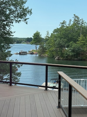 A wooden deck with a railing overlooking a calm river, surrounded by trees and a clear sky. - Mainland St. Lawrence River Home with Private Dock (Alexandria Bay)