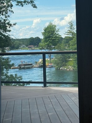 A view from a balcony overlooking a river with boats, trees, and houses in the background. - Mainland St. Lawrence River Home with Private Dock (Alexandria Bay)