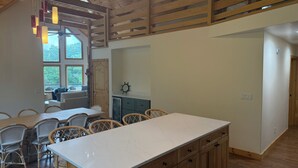 Cozinha ampla com uma ilha grande, vigas de madeira no teto e vista para o exterior através de grandes janelas.