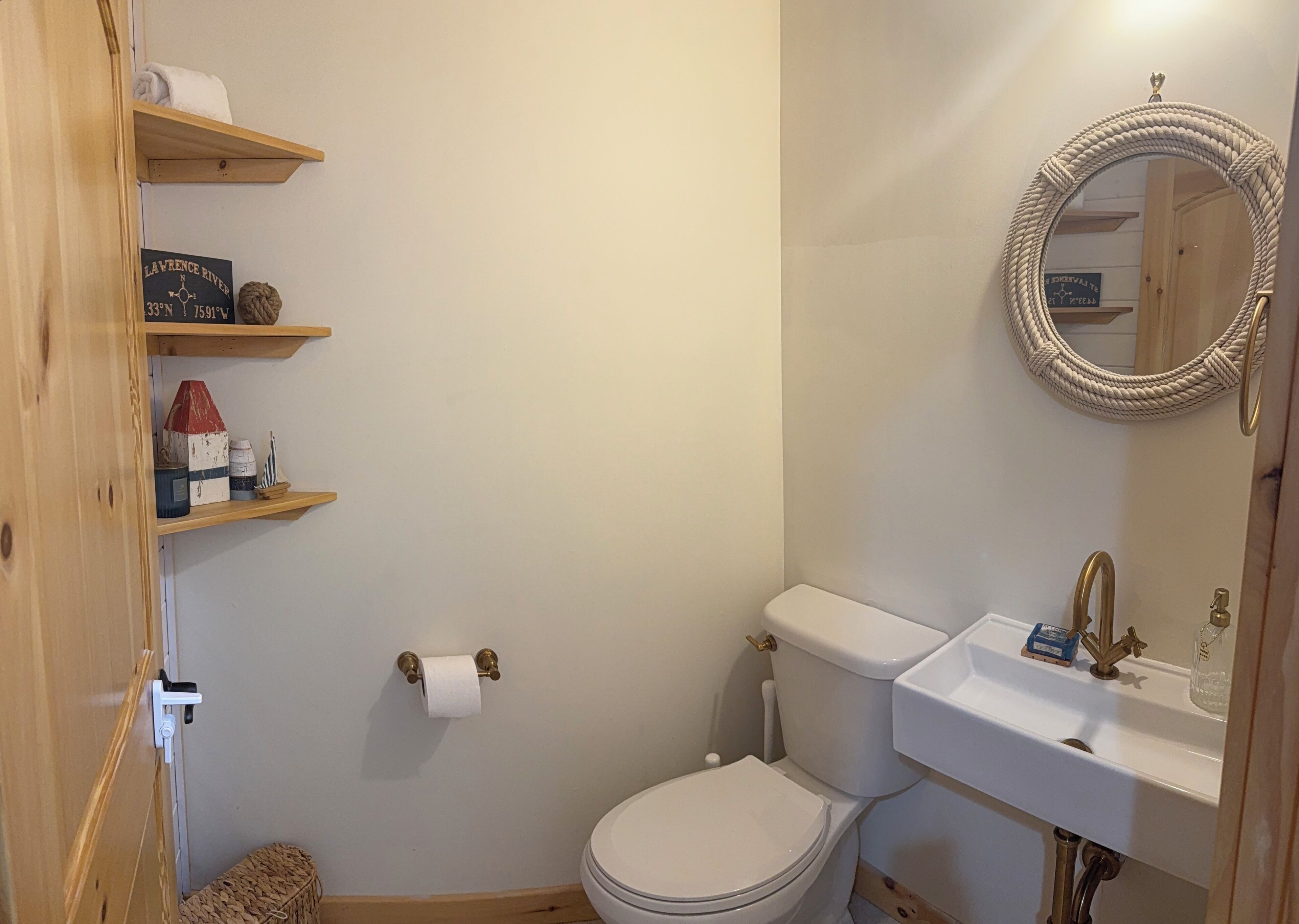 A bathroom with a toilet, sink, and shelves with various items.