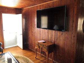 A room with wooden panel walls, a flat-screen TV mounted on the wall, a wooden side table with drawers, and a glass coffee table with a tissue box. - The Retreat of BlackBeard (Kitty Hawk)