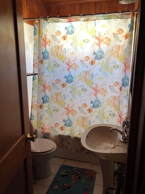 Une salle de bain avec un rideau de douche orné d’un motif de poissons, des toilettes, un lavabo et un tapis décoré de motifs de poissons.