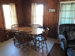 A wooden dining room with a round table and six chairs. There is a sign on the wall that reads "The Bar". - The Retreat of BlackBeard (Kitty Hawk)