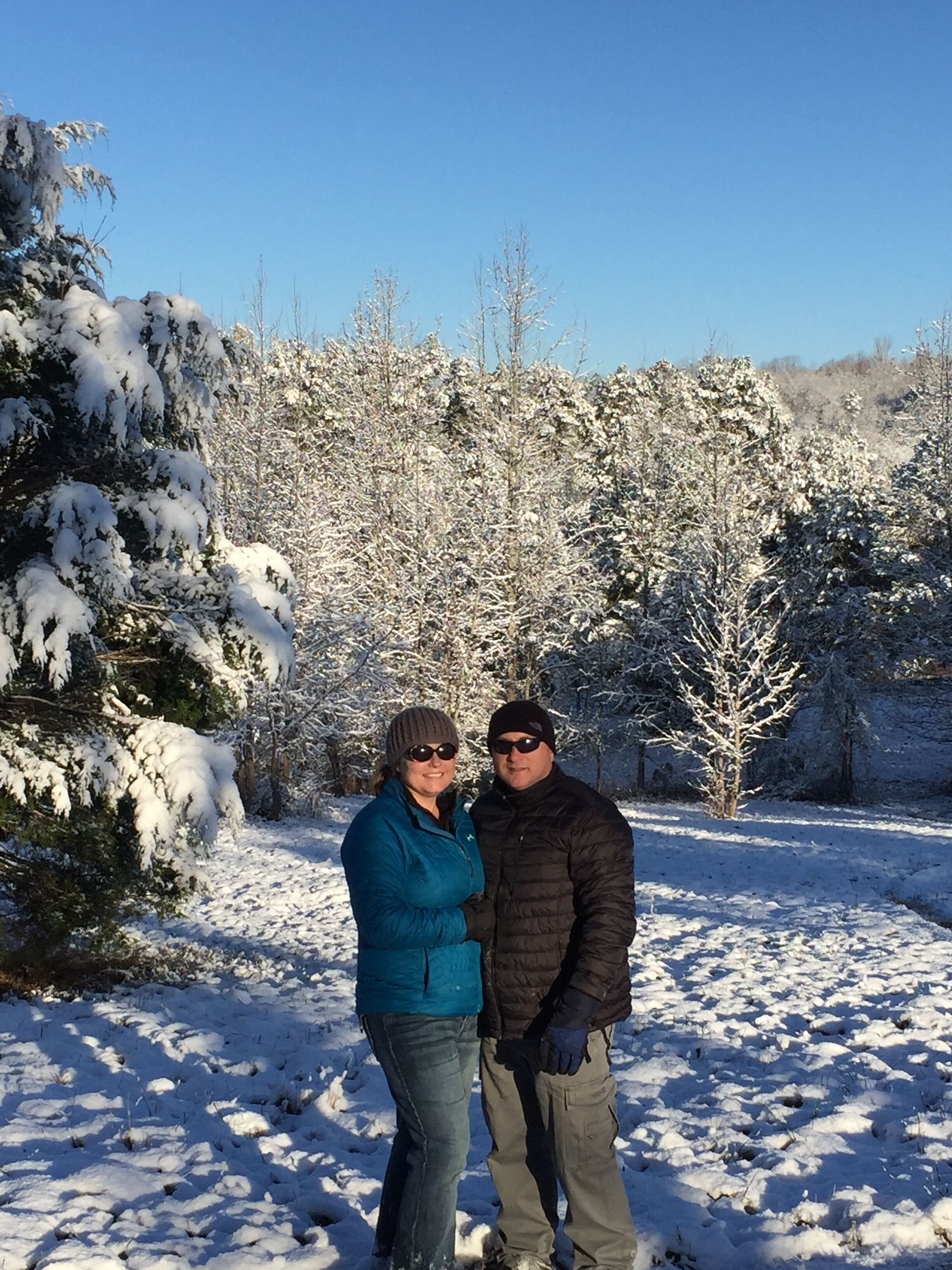 A couple standing in a snowy landscape with trees in the background.
