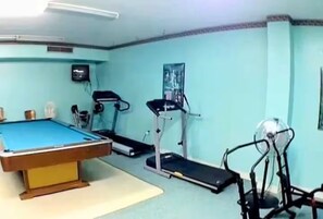Una habitación con mesa de billar, equipo de ejercicios y cinta de correr.
