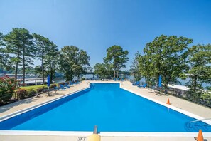 A rectangular swimming pool with a clear blue water surface, surrounded by a deck with lounge chairs and umbrellas, and trees in the background. - Cozy and Chic Coastal 1 Bedroom Condo in Hotspring with  Balcony Views (Hot Springs)