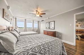 A bedroom with a large bed, a ceiling fan, a dresser, and a view of the outdoors. - Cozy and Chic Coastal 1 Bedroom Condo in Hotspring with  Balcony Views (Hot Springs)