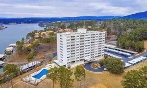A multi-story hotel with a swimming pool, surrounded by trees and a body of water. - Cozy and Chic Coastal 1 Bedroom Condo in Hotspring with  Balcony Views (Hot Springs)