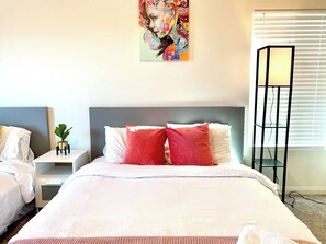 Een hotelkamer met een bed, een nachtkastje met een plant, een kunstwerk aan de muur en een vloerlamp.