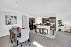 Een moderne keuken met een centraal kookeiland, barstoelen en een eethoek met een tafel en stoelen.