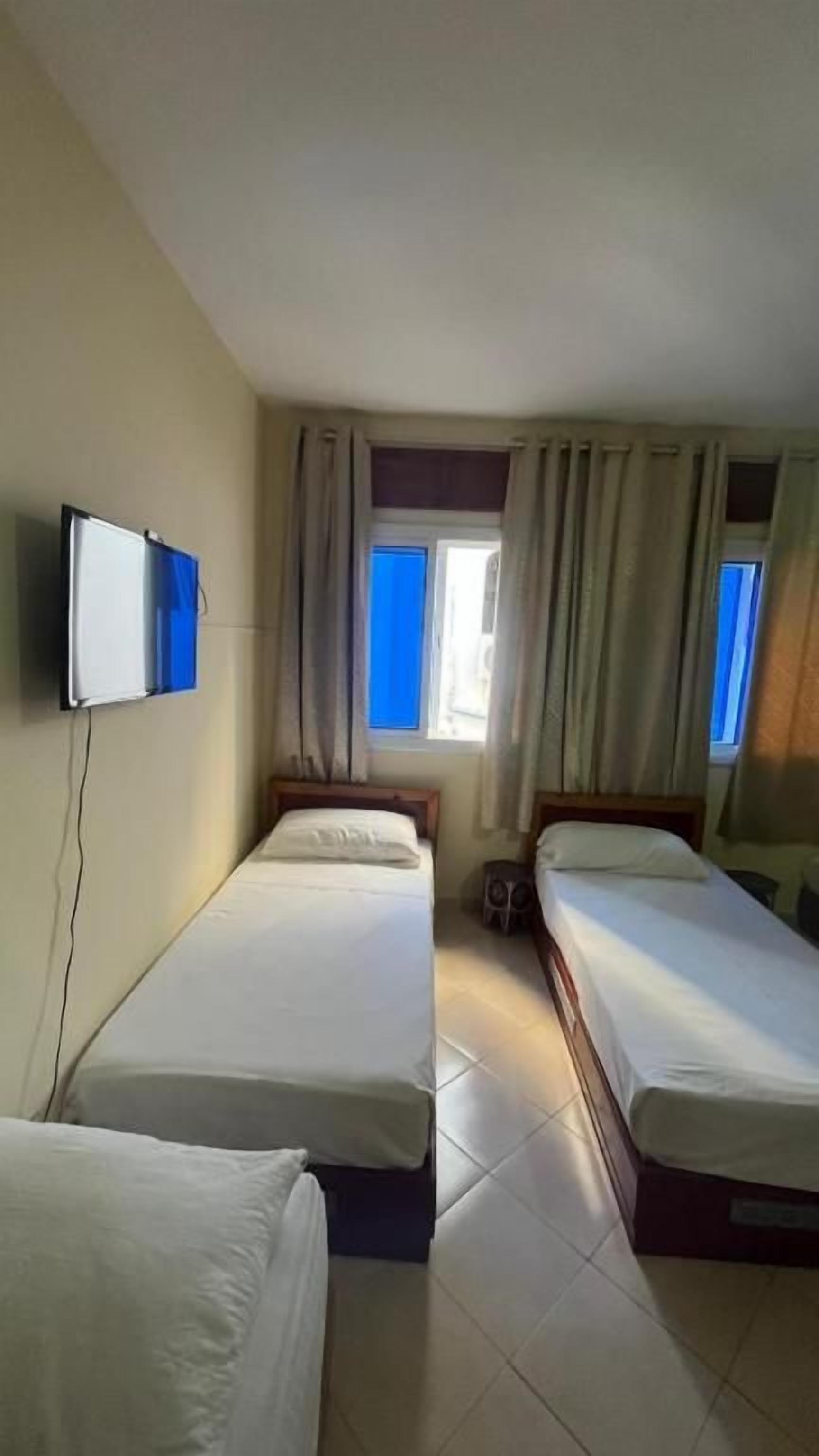 Une chambre d’hôtel avec deux lits simples, un téléviseur fixé au mur et une fenêtre avec des rideaux.