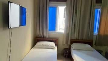Une chambre d’hôtel avec deux lits simples, un téléviseur fixé au mur et une fenêtre avec des rideaux.
