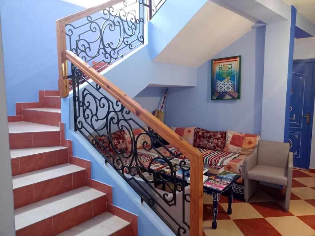A staircase with ornate metal railings, a sofa with patterned cushions, and a blue door in a room with a checkered floor.