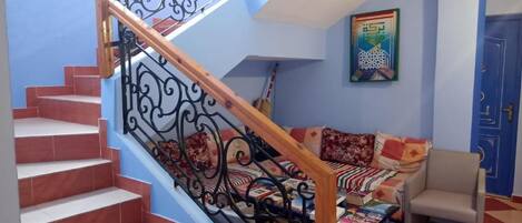 A staircase with ornate metal railings, a sofa with patterned cushions, and a blue door in a room with a checkered floor.