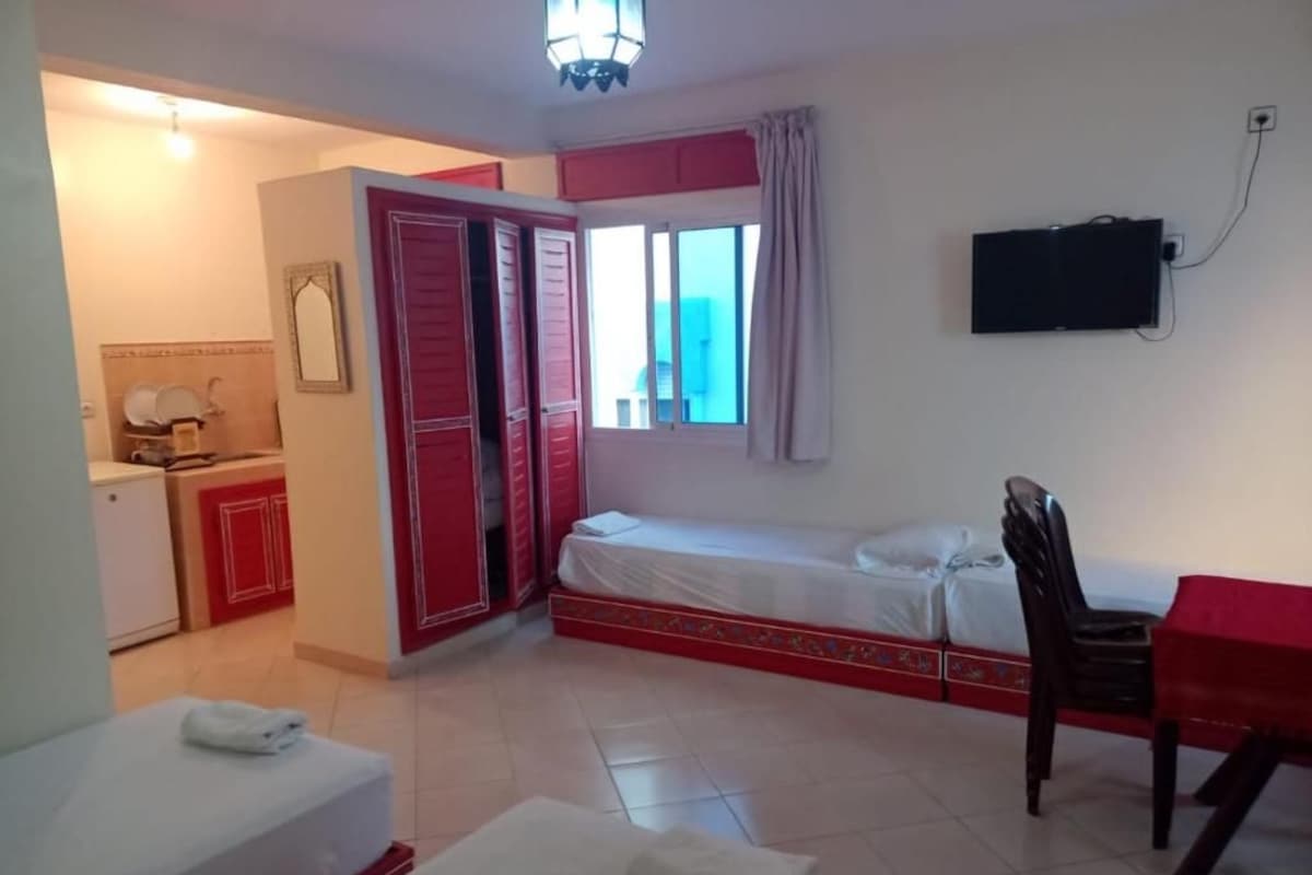 A hotel room with a bed, a desk, a chair, a TV, and a bathroom with a toilet and sink.