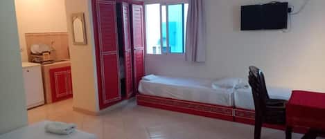 A hotel room with a bed, a desk, a chair, a TV, and a bathroom with a toilet and sink.