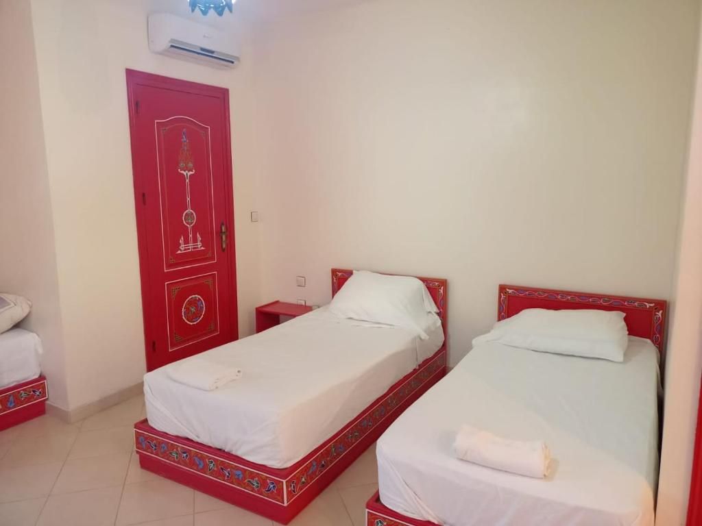 A room with two beds, a red door, and an air conditioning unit.
