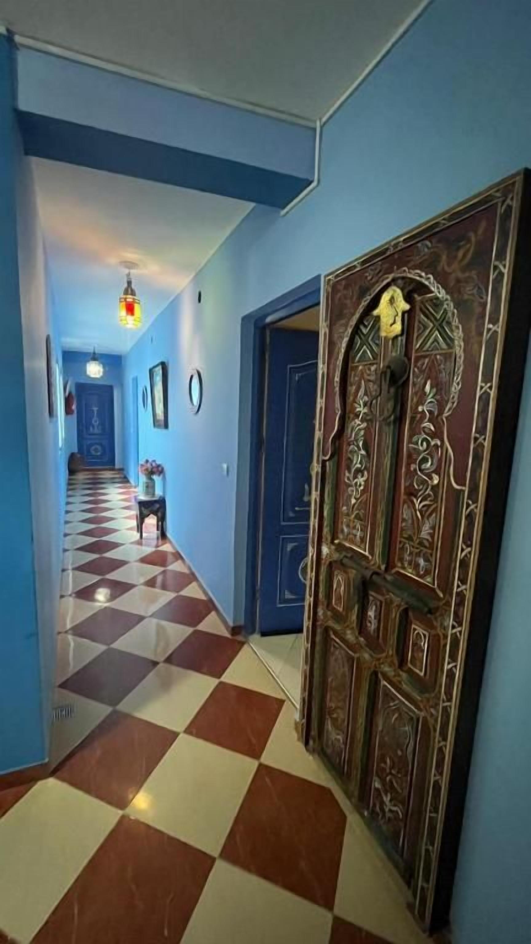 A hallway with a checkered floor, a decorative door, and a hanging light fixture.