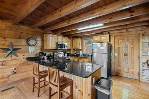Ein Holzblockhaus-Interieur mit einer Küche, die eine zentrale Kochinsel, Holzschränke und einen Edelstahl-Kühlschrank zeigt.