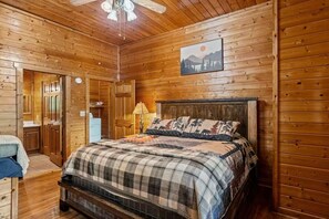 Ein Schlafzimmer einer Holzhütte mit Bett, Nachttisch, Lampe und einem Gemälde an der Wand.