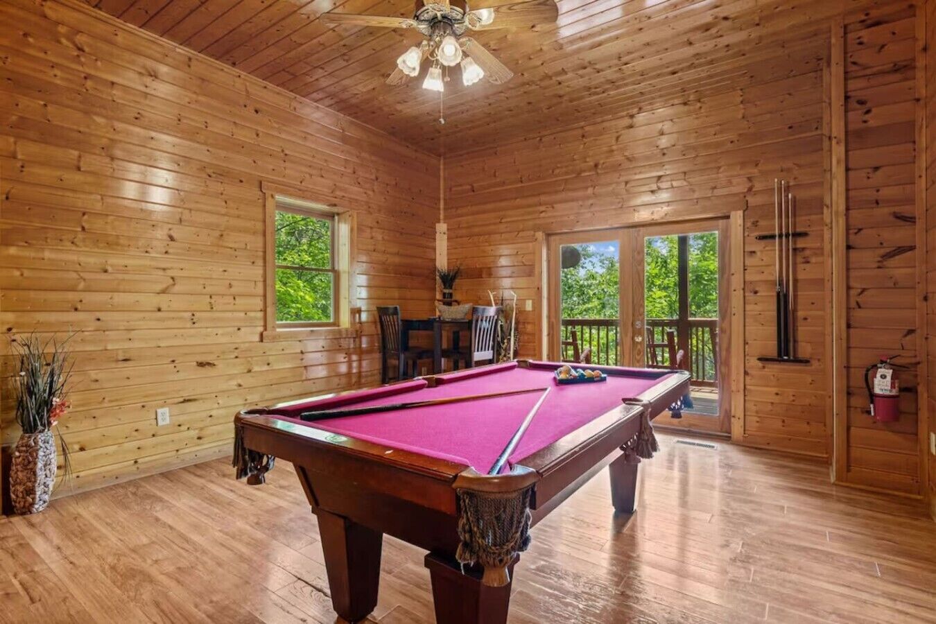 A wooden interior with a pool table, windows, and a ceiling fan.