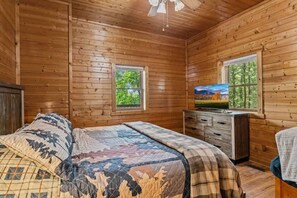 A wooden cabin bedroom with a bed, a dresser, a television, and two windows. - Epic Views | Hot Tub | Minutes to Pigeon Forge (Sevierville)