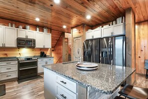 A kitchen with granite countertops, stainless steel appliances, and wooden paneling. - Luxury8bdrmCabin-LgPool-HotTub-5MinParkway-Special (Sevierville)