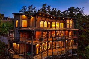 A multi-level wooden cabin with a hot tub and outdoor seating area. - Luxury8bdrmCabin-LgPool-HotTub-5MinParkway-Special (Sevierville)