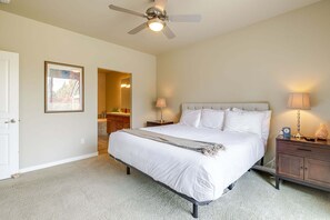 A bedroom with a bed, bedside lamps, a nightstand, a ceiling fan, and a door leading to a bathroom.