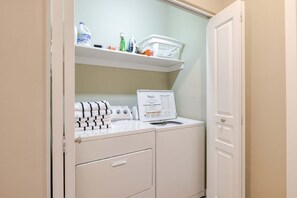 A laundry room with a washer and dryer, a shelf with cleaning supplies, and a door.