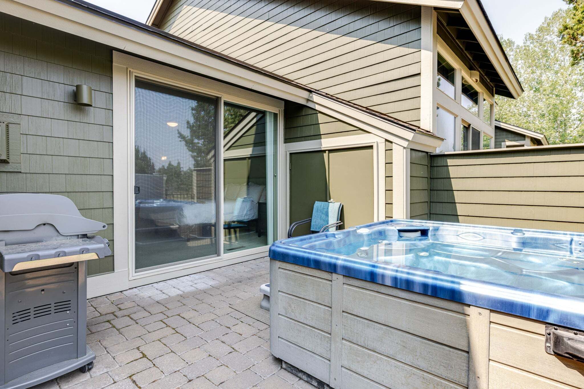 A backyard with a hot tub, a grill, and a sliding glass door leading to a covered patio area.
