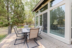 An outdoor patio with a table and chairs, surrounded by a fence and trees.