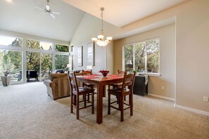 A dining area with a wooden table and chairs, a ceiling fan, and large windows with blinds.