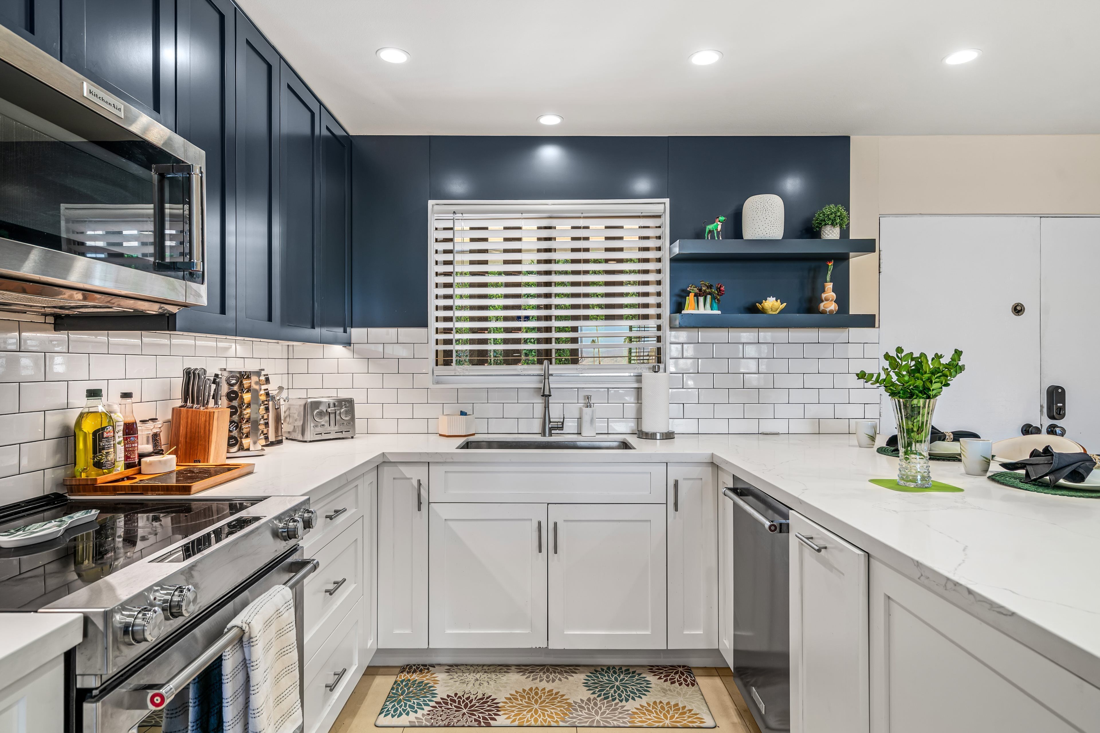 A modern kitchen with white cabinetry, a stainless steel range, and a window with blinds.