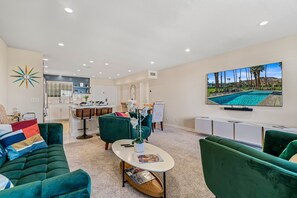 A modern living room with a green sofa, a coffee table, and a TV displaying a pool view. - Desert Elegance Off El Paseo (Palm Desert)