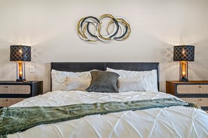 A neatly made bed with a white duvet and multiple pillows, flanked by two bedside tables with lamps, and a wall art piece above. - Desert Elegance Off El Paseo (Palm Desert)