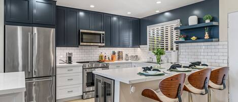 A modern kitchen with dark cabinets, stainless steel appliances, and a central island with bar stools.