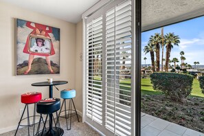 A room with a large window, a painting on the wall, and a view of palm trees and a garden. - Desert Elegance Off El Paseo (Palm Desert)