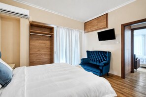 Ein Hotelzimmer mit einem Bett, einem blauen Sessel, einem Kleiderschrank, einem Flachbildfernseher und einer Schiebetür zu einem Balkon.