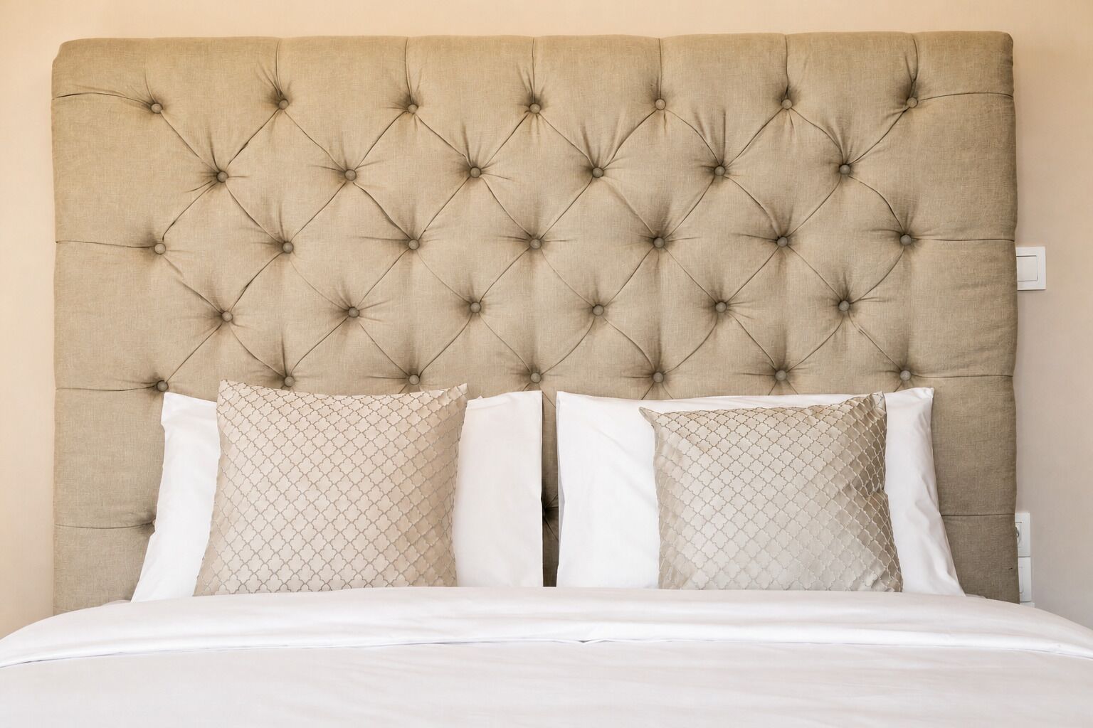 Un lit avec une tête de lit capitonnée, deux oreillers et un couvre-lit blanc.