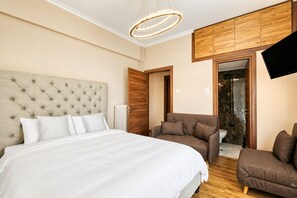 Une chambre dotée d’un grand lit, d’une armoire en bois, d’un coin salon avec un canapé et un fauteuil, et d’un téléviseur fixé au mur.