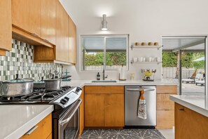 A modern kitchen with wooden cabinets, a gas stove, a dishwasher, and a window with a view of greenery. - The Orchid Tree Inn, Est. in 2026, Central Palm Springs, A Mid-Century Beauty (Palm Springs)