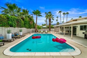 A rectangular swimming pool with two red floating toys, surrounded by palm trees and a covered patio area. - The Orchid Tree Inn, Est. in 2026, Central Palm Springs, A Mid-Century Beauty (Palm Springs)