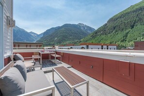 Een terras op het dak met buitenmeubels, een tafel en uitzicht op bergen.