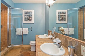 Een badkamer met een douchecabine van glas, twee wastafels, een toilet en een grote spiegel.