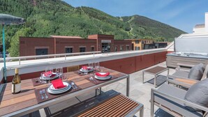 An outdoor dining area with tables set for two, a hot tub, and a view of a forested hillside. - Diamondtooth 3 3 Bedroom/ 3 Bathroom Downlown Condo (Telluride)