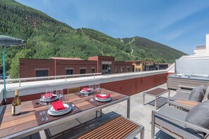 Een buitenterras met tafels voor twee personen, een jacuzzi en uitzicht op een bebost glooiend landschap.