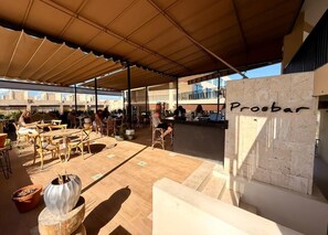 Een terras met tafels en stoelen, een bar en een stenen muur met de tekst 'Proebar'.